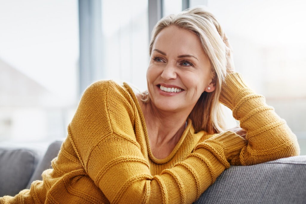 Middle aged blonde woman smiling on sofa looking off to the side